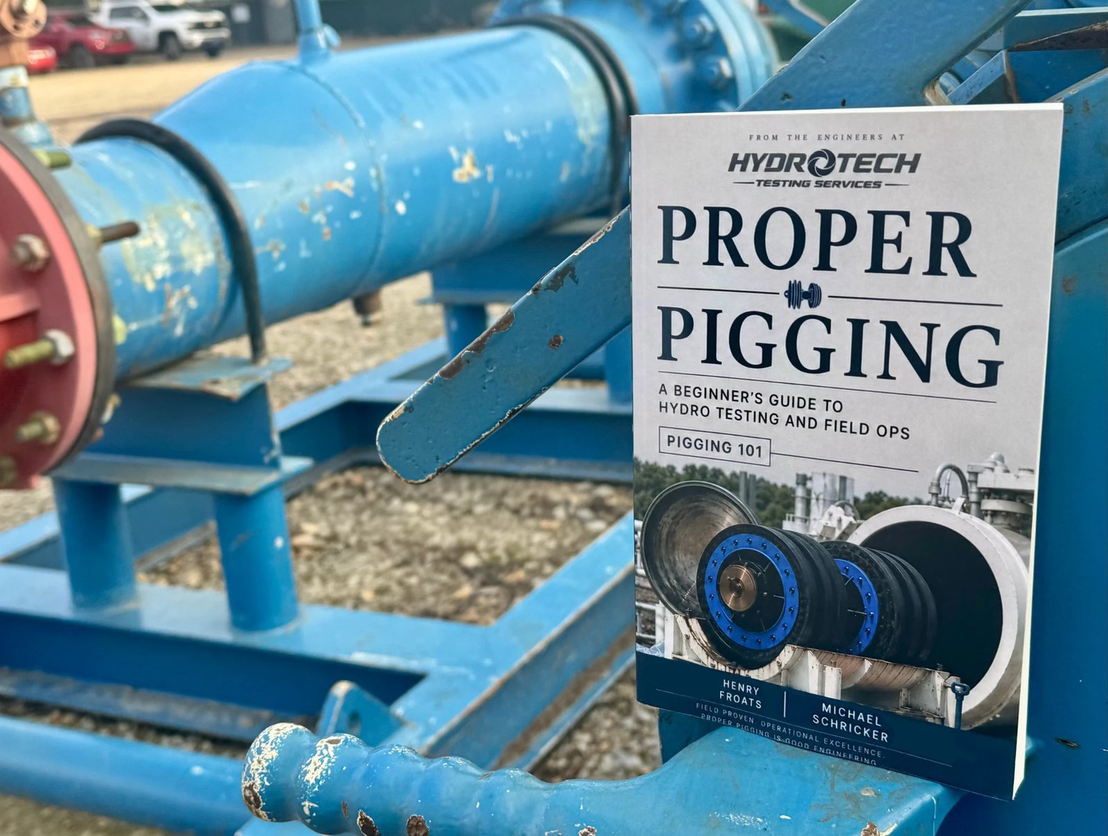 The printed Proper Pigging field guide propped on a skid-mounted pig launcher and receiver barrel at a pipeline yard.